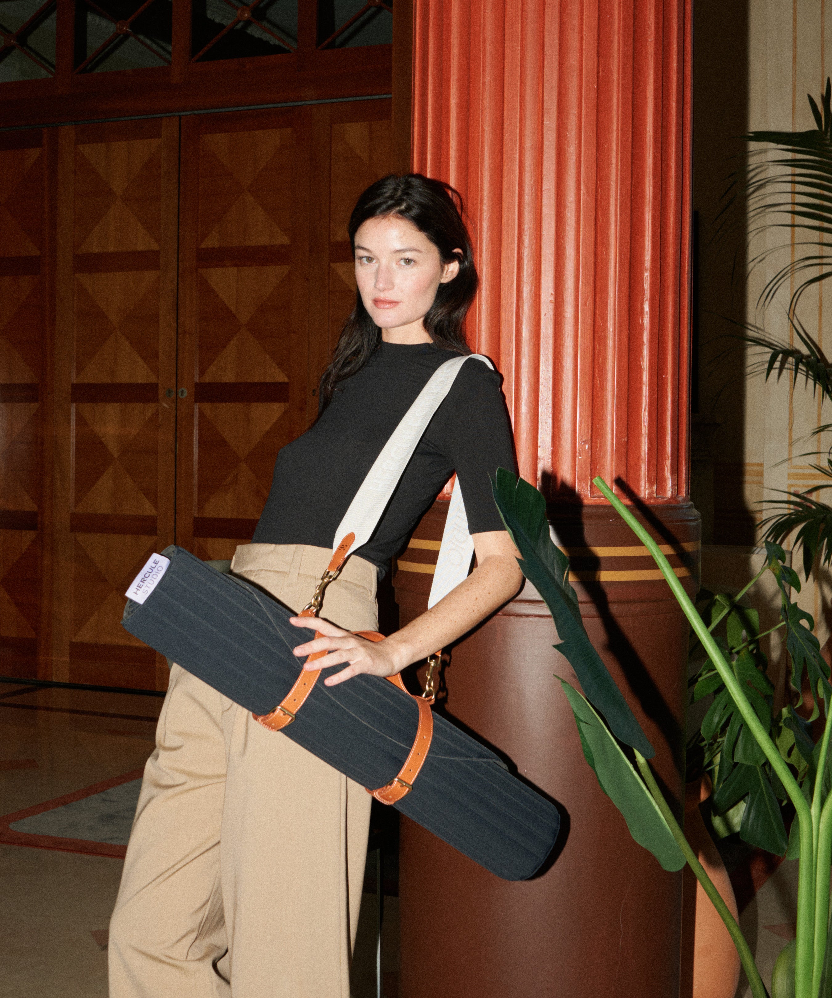 Tapis de sport couleur Outrenoir de la marque Hercule Studio avec sangle de stransport Soca en cuir végétal photo lifestyle avec mannequin