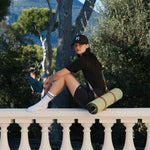 Tapis de sport couleur Pistache de la marque Hercule Studio avec sangle de transport Soca en cuir végétal photo lifestyle avec mannequin sur balcon