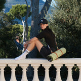 Tapis de sport couleur Pistache de la marque Hercule Studio avec sangle de transport Soca en cuir végétal photo lifestyle avec mannequin sur balcon
