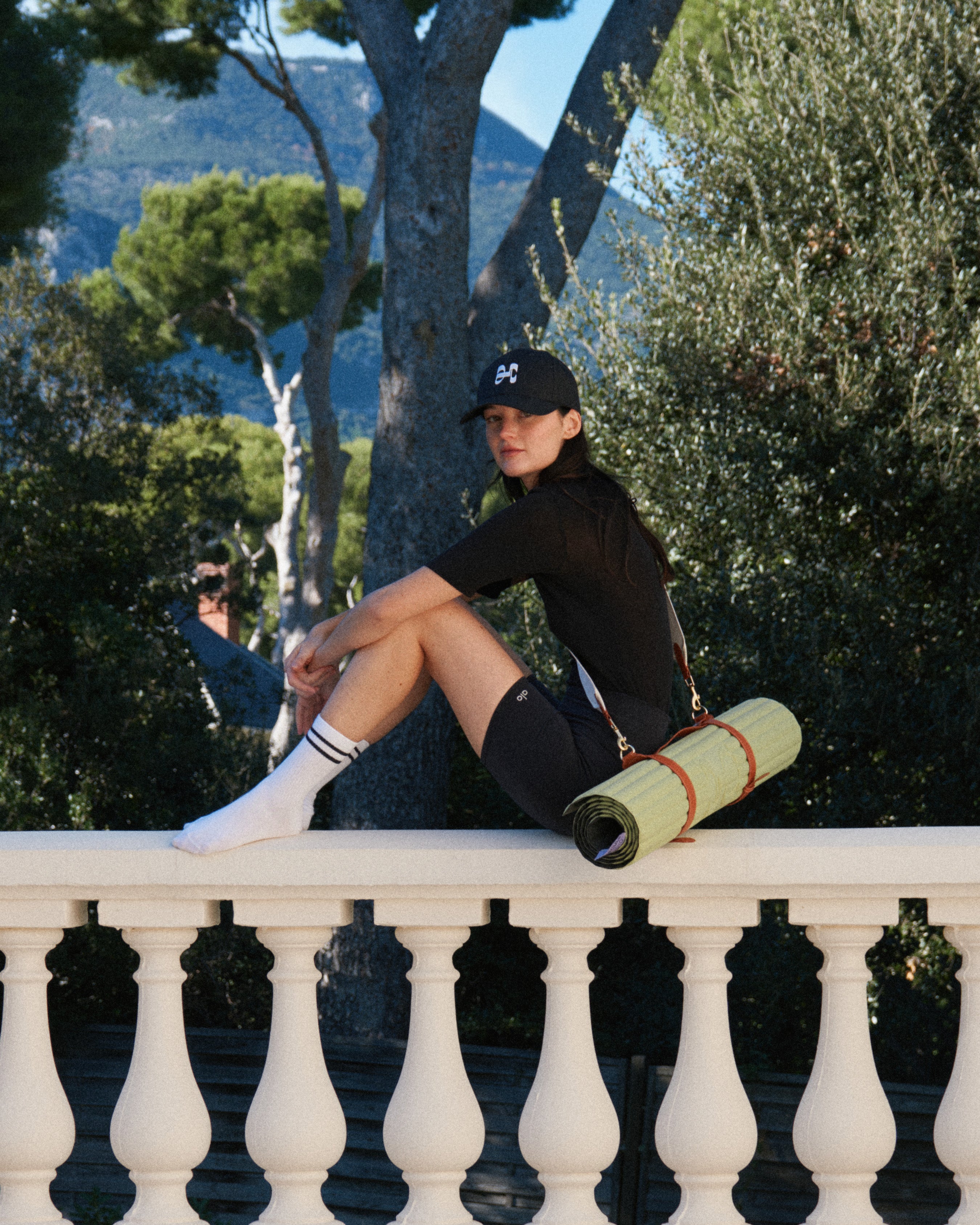 Tapis de sport couleur Pistache de la marque Hercule Studio avec sangle de transport Soca en cuir végétal photo lifestyle avec mannequin sur balcon
