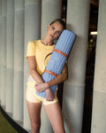 Hercule Studio Archy Blue Jean exercise mat in a lifestyle setting with a model and a carrying strap for the mat, featuring a minimalist blue color perfect for Pilates and gym classes, with a durable French design