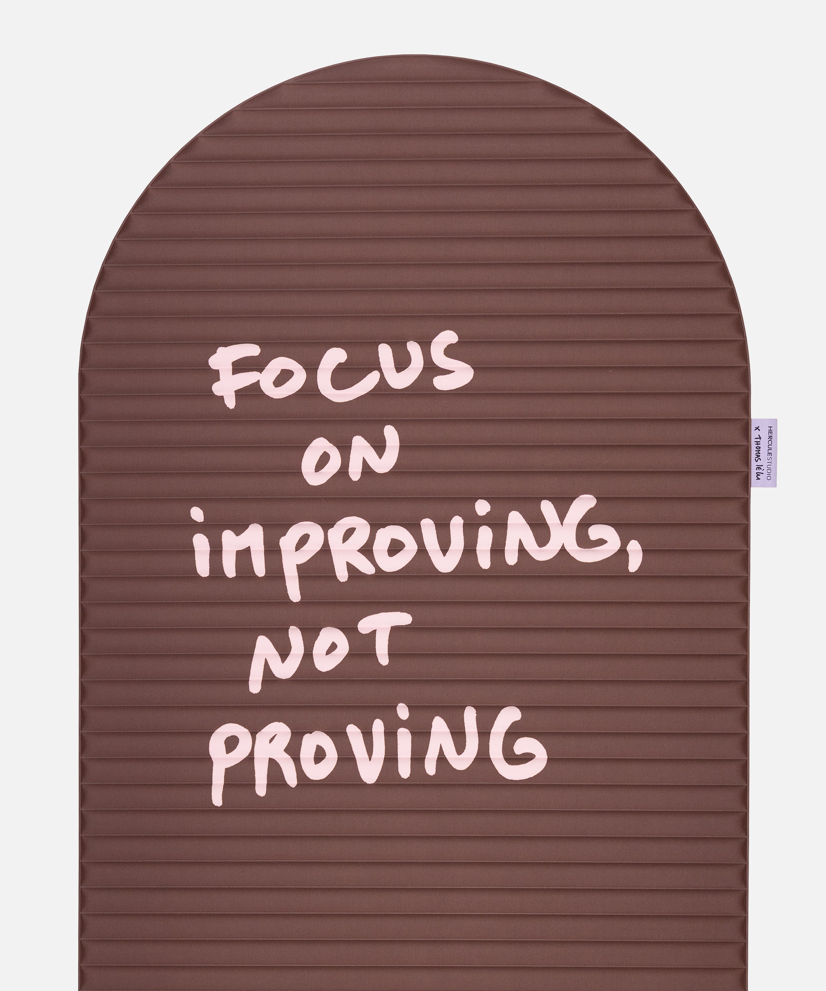 Close-up on the pink quote “focus on improving not proving” on the Hercule Studio x Thomas Lélu sport mat, artistic message and graphic typography