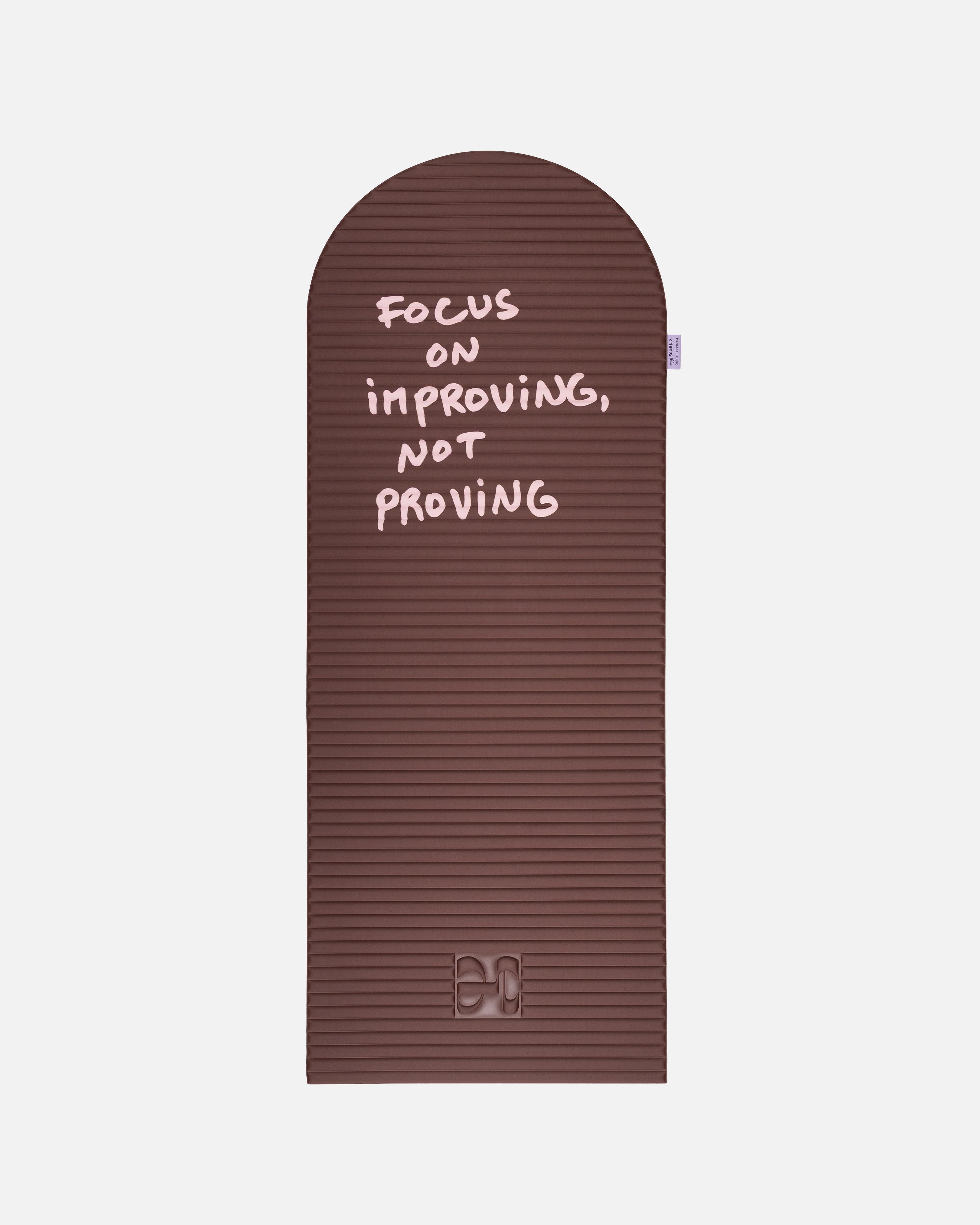 Hercule Studio x Thomas Lélu Limited Edition Exercise Mat, brown designer floor mat featuring a pink quote reading “focus on improving not proving,” an artistic collaboration for fitness, Pilates, and stretching, unfolded view