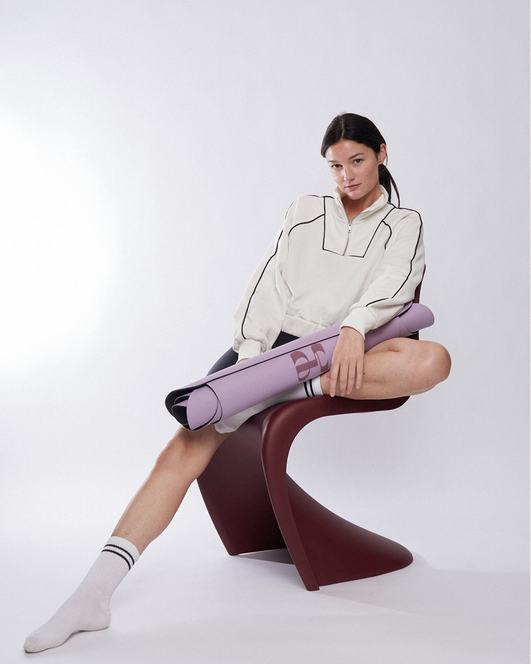 Tapis de sol pour le yoga de la marque hercule studio modèle mar couleur lavande tenu par un mannequin assis sur fond blanc