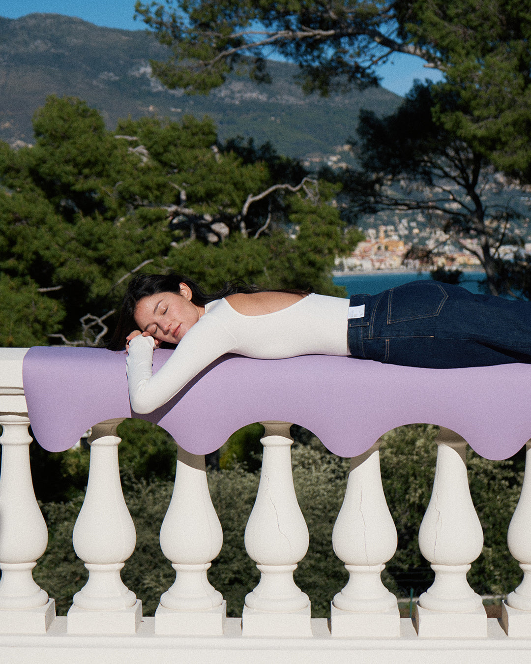 Tapis de sol pour le yoga de la marque hercule studio modèle mar couleur lavande lifestyle avec mannequin allongé sur le rebord du balcon