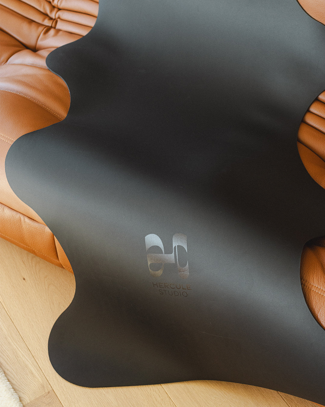 Tapis de sol pour le yoga de la marque hercule studio modèle mar couleur outrenoir photo lifestyle zoom logo photo sur canapé en cuir marron